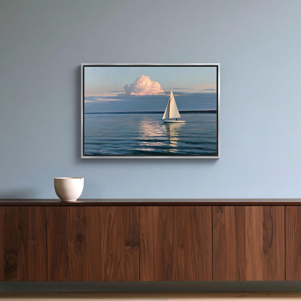 Sailboat at dusk canvas wall art, framed painting of a sailboat on the water hangs on a blue wall above a wooden cabinet