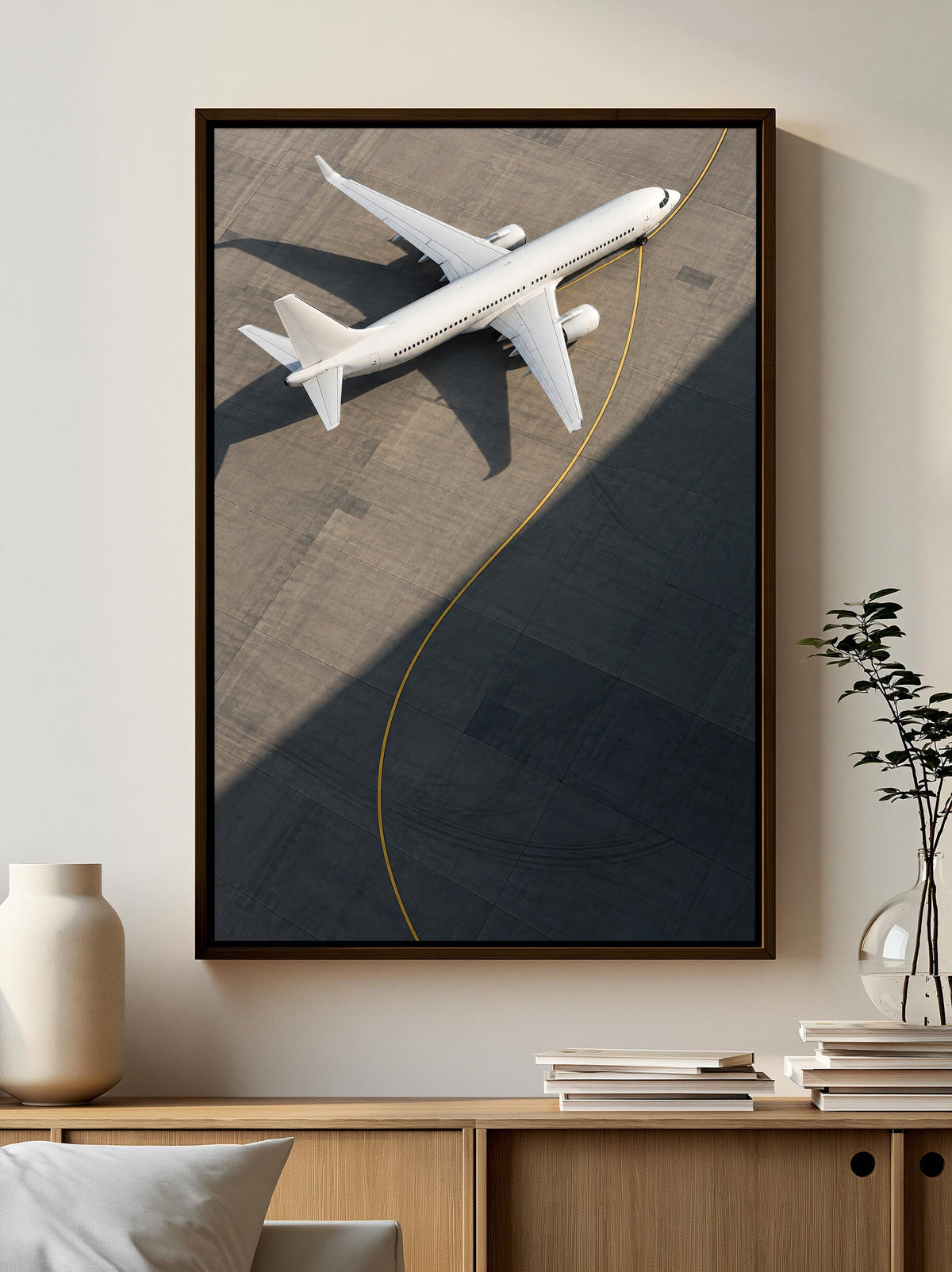 A framed photograph of a white airplane on an airport tarmac is displayed on a wall, with a wooden cabinet and a plant in the foreground.