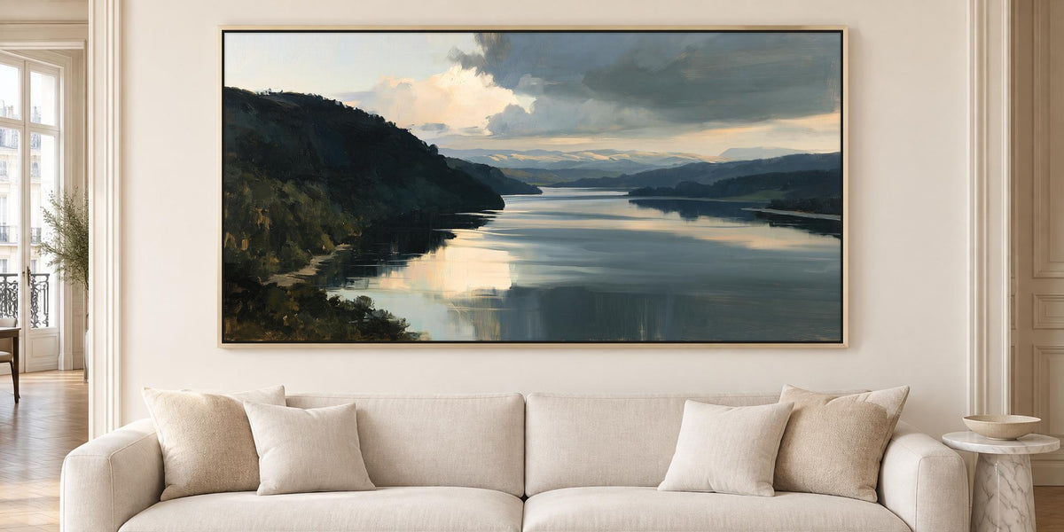 a large landscape painting hanging on a wall above a beige sofa with white pillows.