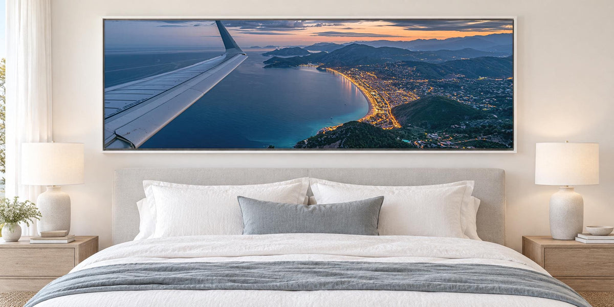 a large, framed picture of an aerial view of a coastal city at sunset, with the wing of an airplane visible in the top left corner.
