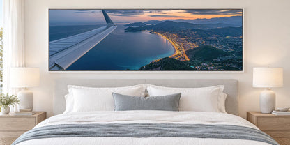 a large, framed picture of an aerial view of a coastal city at sunset, with the wing of an airplane visible in the top left corner.