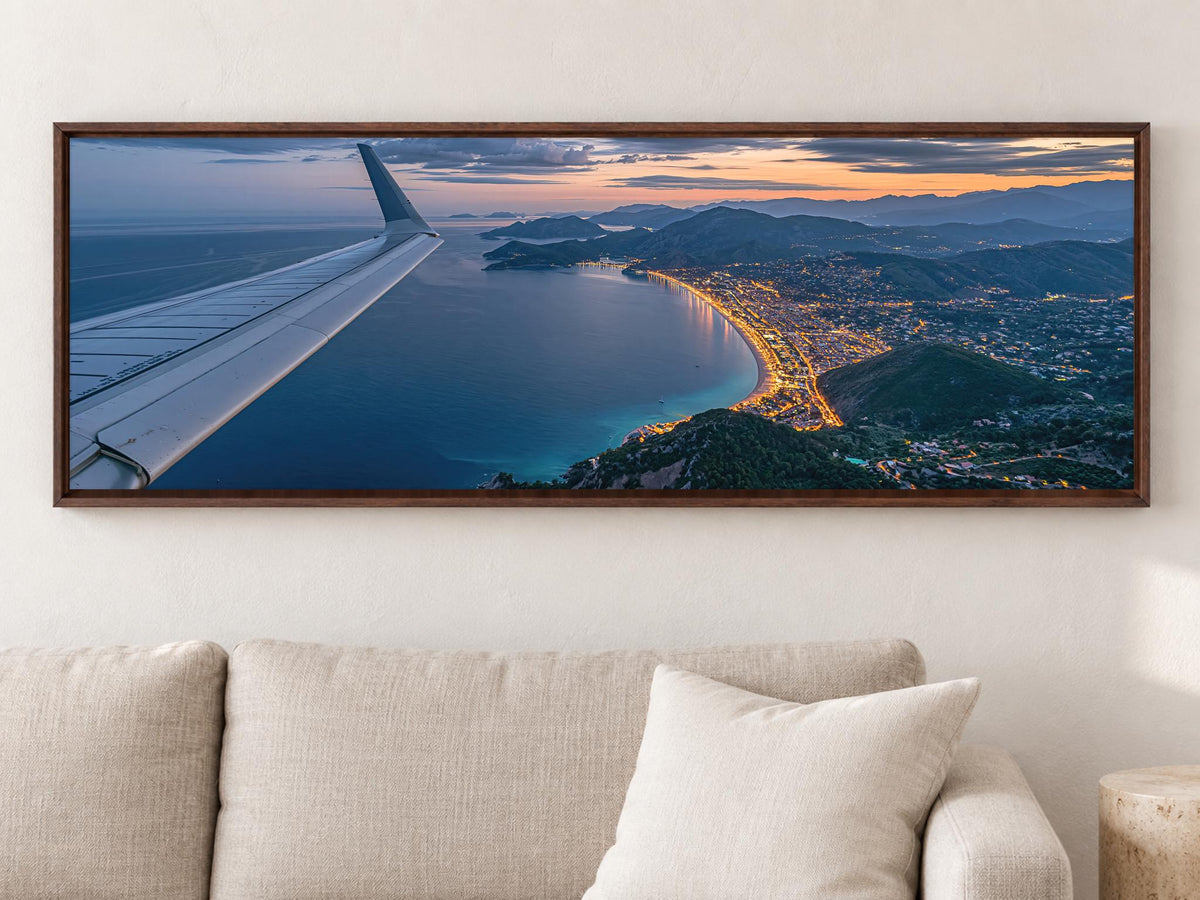 A large framed photograph of an aerial view of a coastal city at sunset, with the wing of an airplane visible in the foreground.