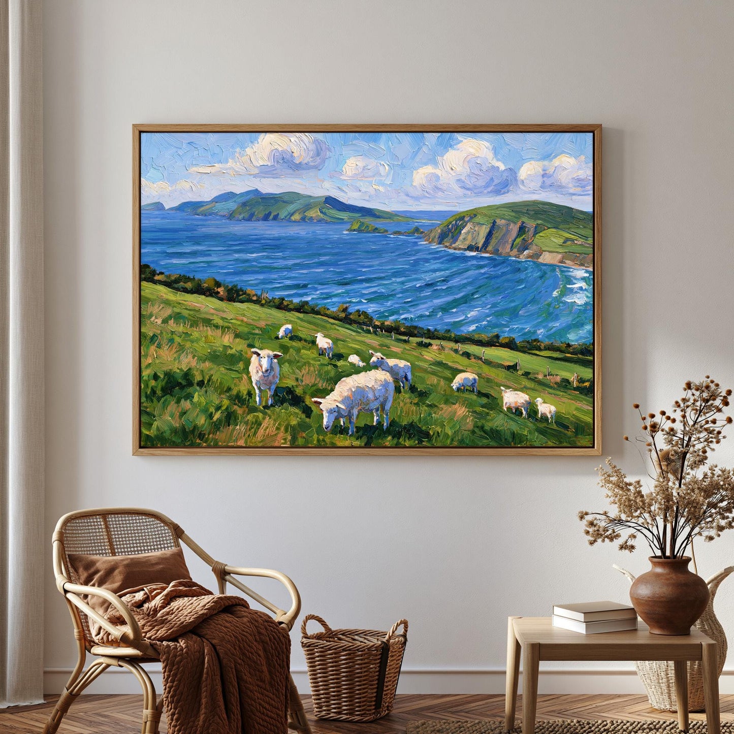 a large painting of a pastoral scene with sheep grazing on a grassy hill overlooking a body of water. The painting is hung on a wall in a room with a wicker chair, a small table with a vase of flowers, and a bookshelf.