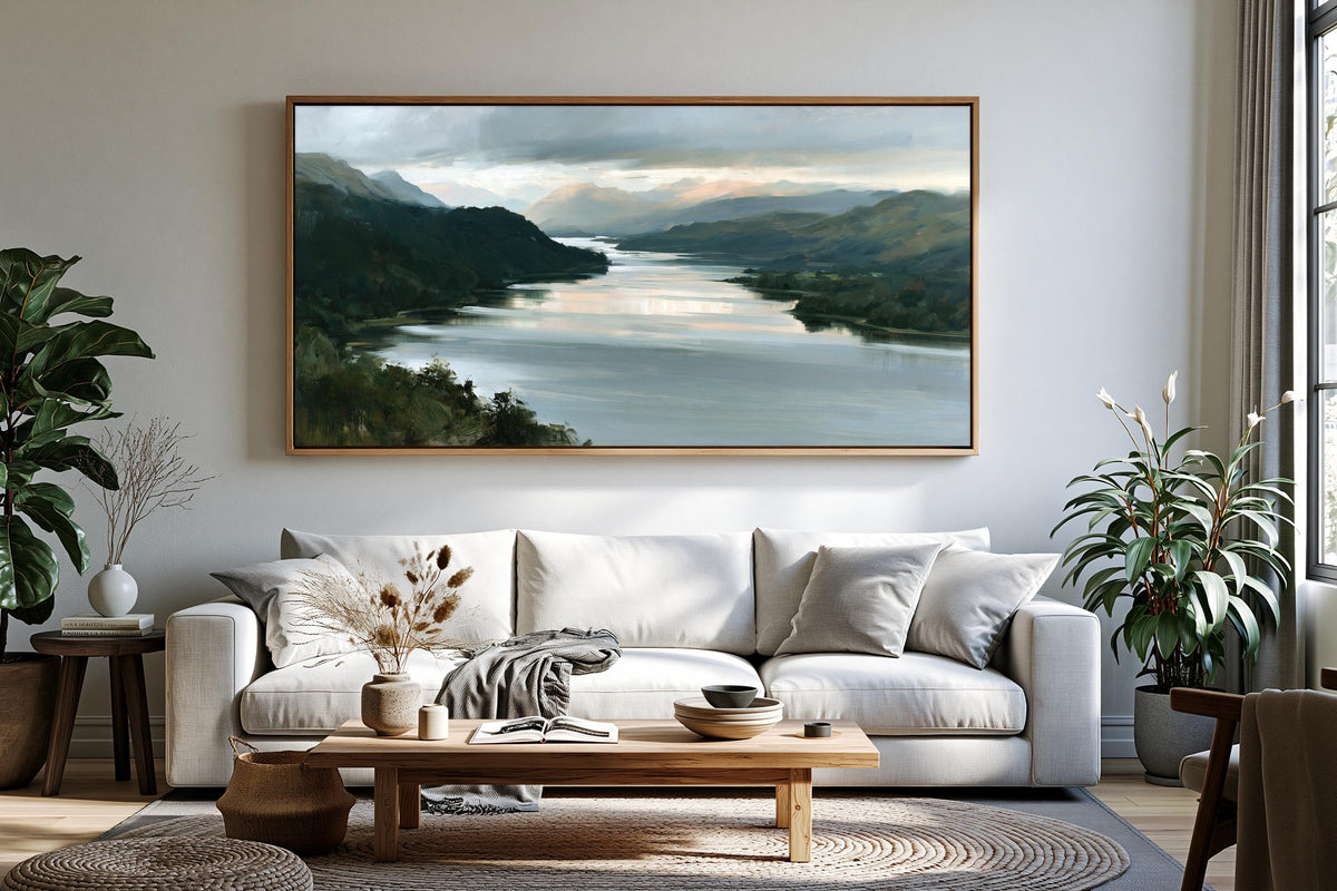 a serene living room with a large landscape painting hanging on the wall above a white sofa. The painting features a tranquil scene of a river surrounded by mountains, creating a peaceful and calming atmosphere.