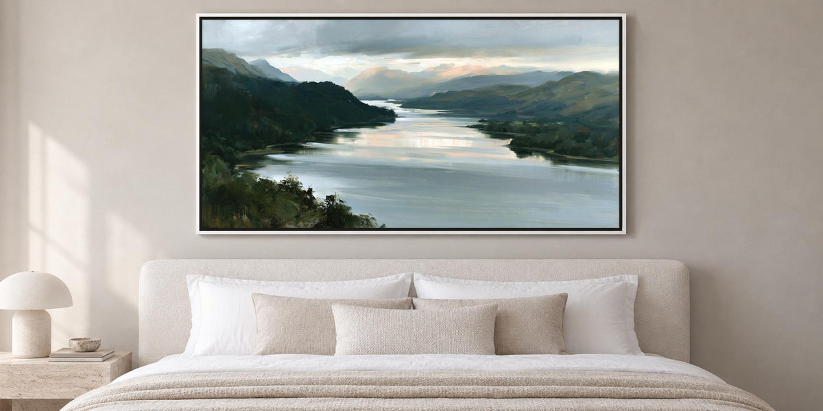 a large painting of a serene landscape with a river and mountains in the background, hanging above a bed with white bedding and pillows.