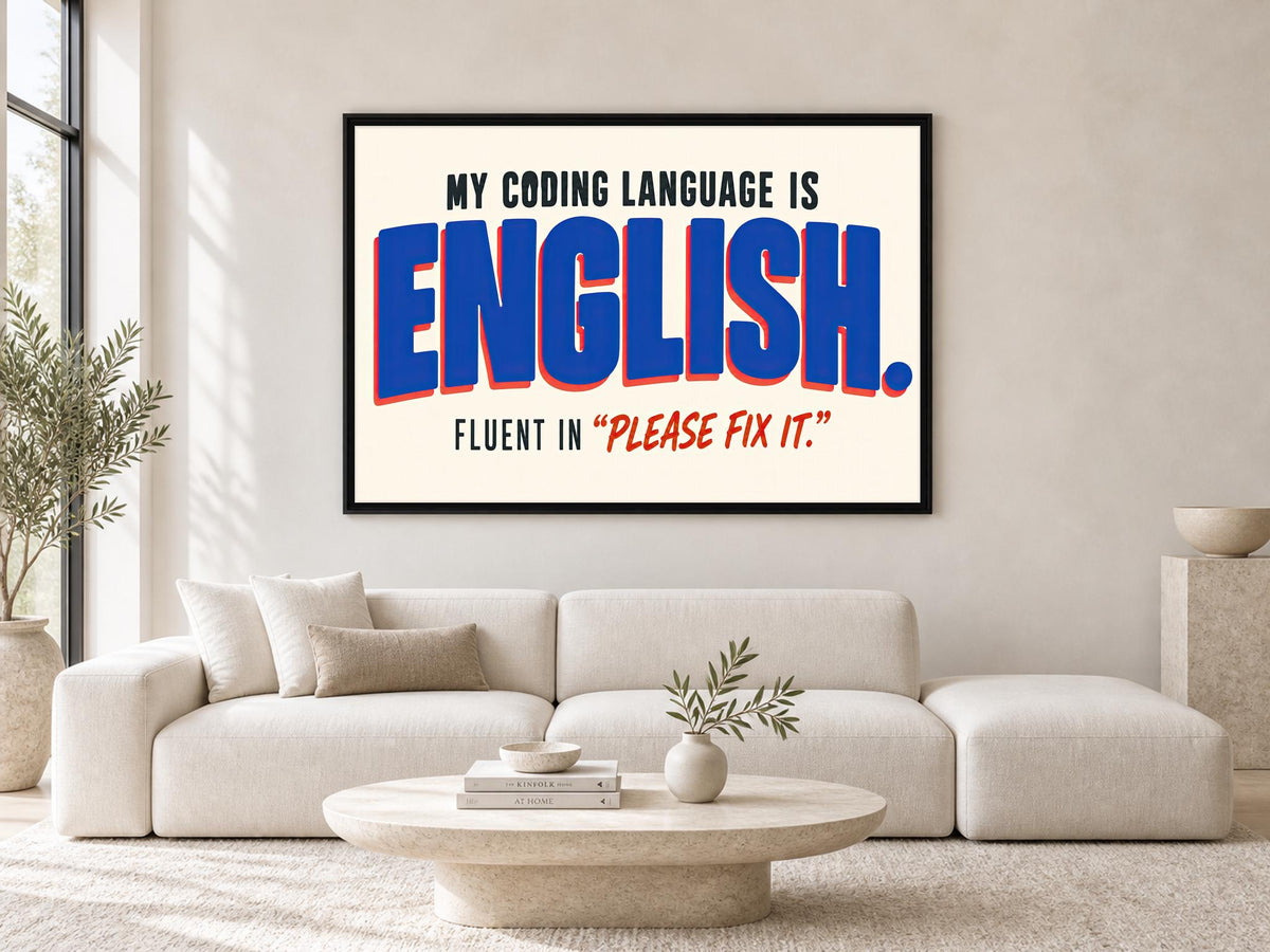 a large framed poster with the text "MY CODING LANGUAGE IS ENGLISH. FLUENT IN "PLEASE FIX IT!"" displayed on a wall above a white sofa in a living room setting.