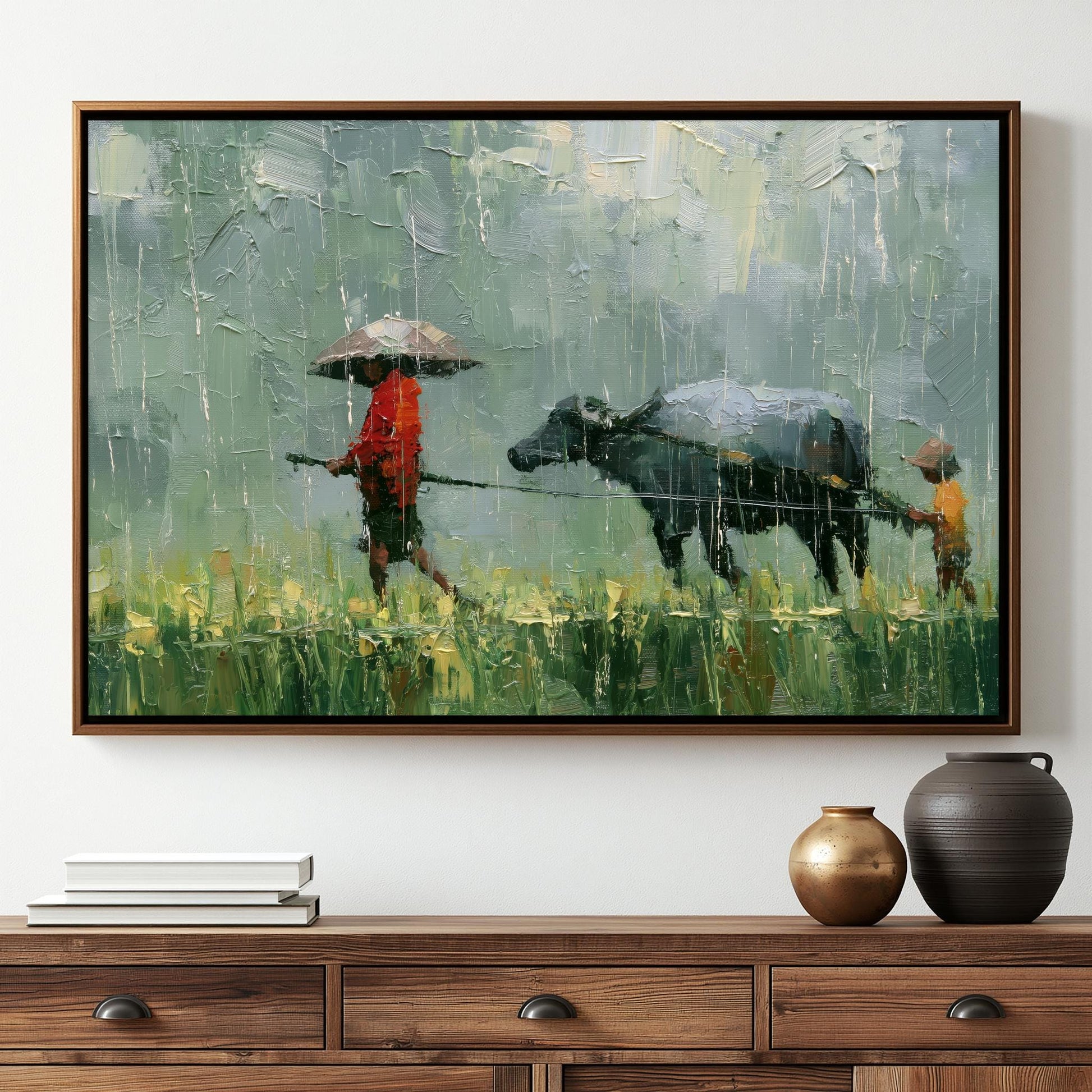 The image is a framed painting depicting a person walking with an umbrella and a cow in a field, with a wooden dresser below it.