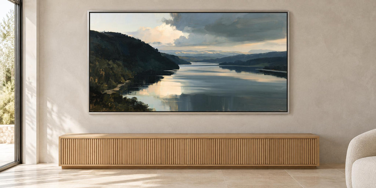 a large painting of a serene landscape with a calm lake and mountains in the background, hanging on a wall above a wooden cabinet or console.