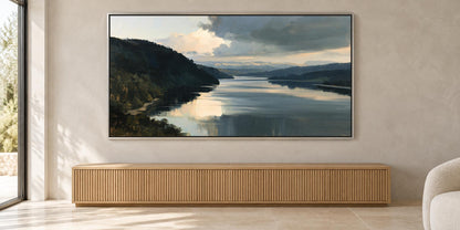a large painting of a serene landscape with a calm lake and mountains in the background, hanging on a wall above a wooden cabinet or console.