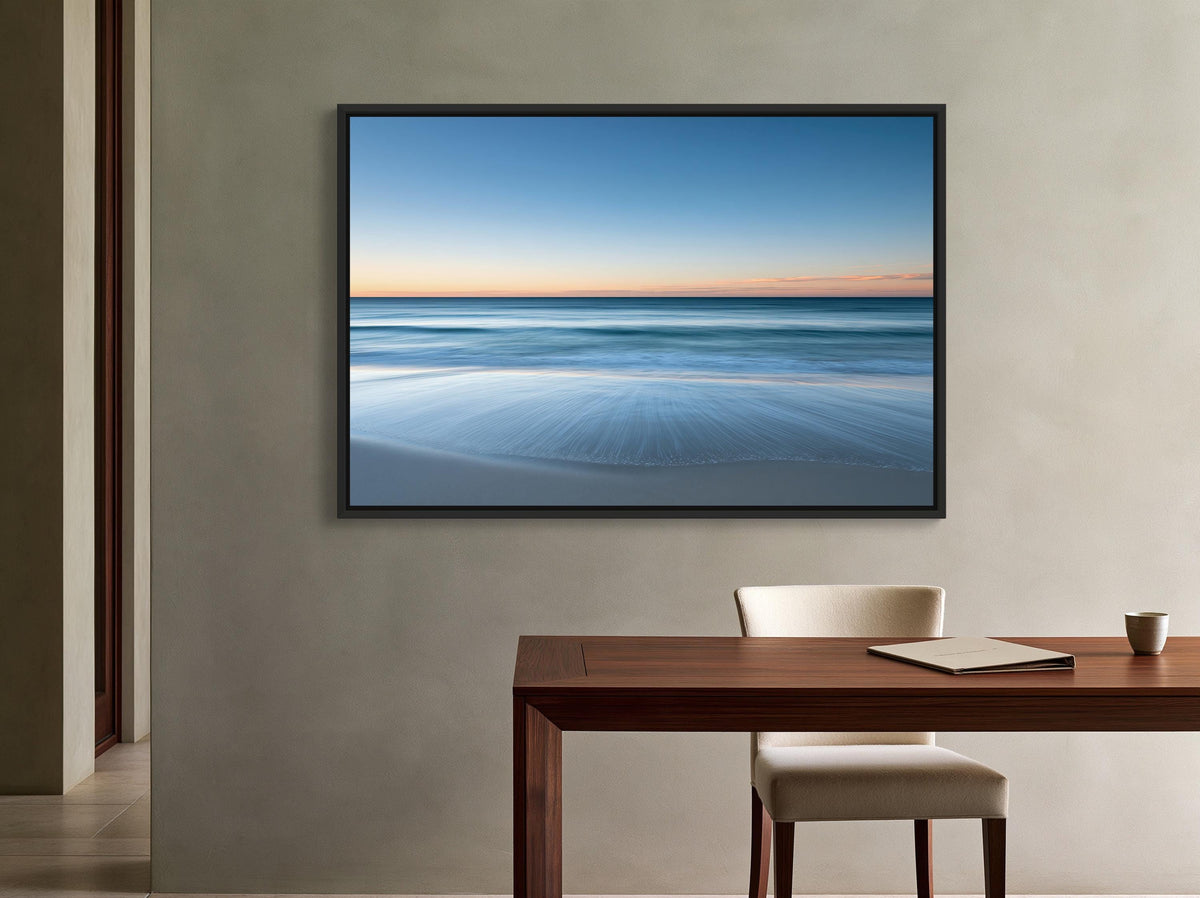 Ocean horizon at dusk canvas wall art, serene beach scene with a wooden table and chair in front of a framed picture of a