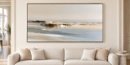 a large, framed painting of a serene landscape hanging on a wall above a beige sofa with two pillows.