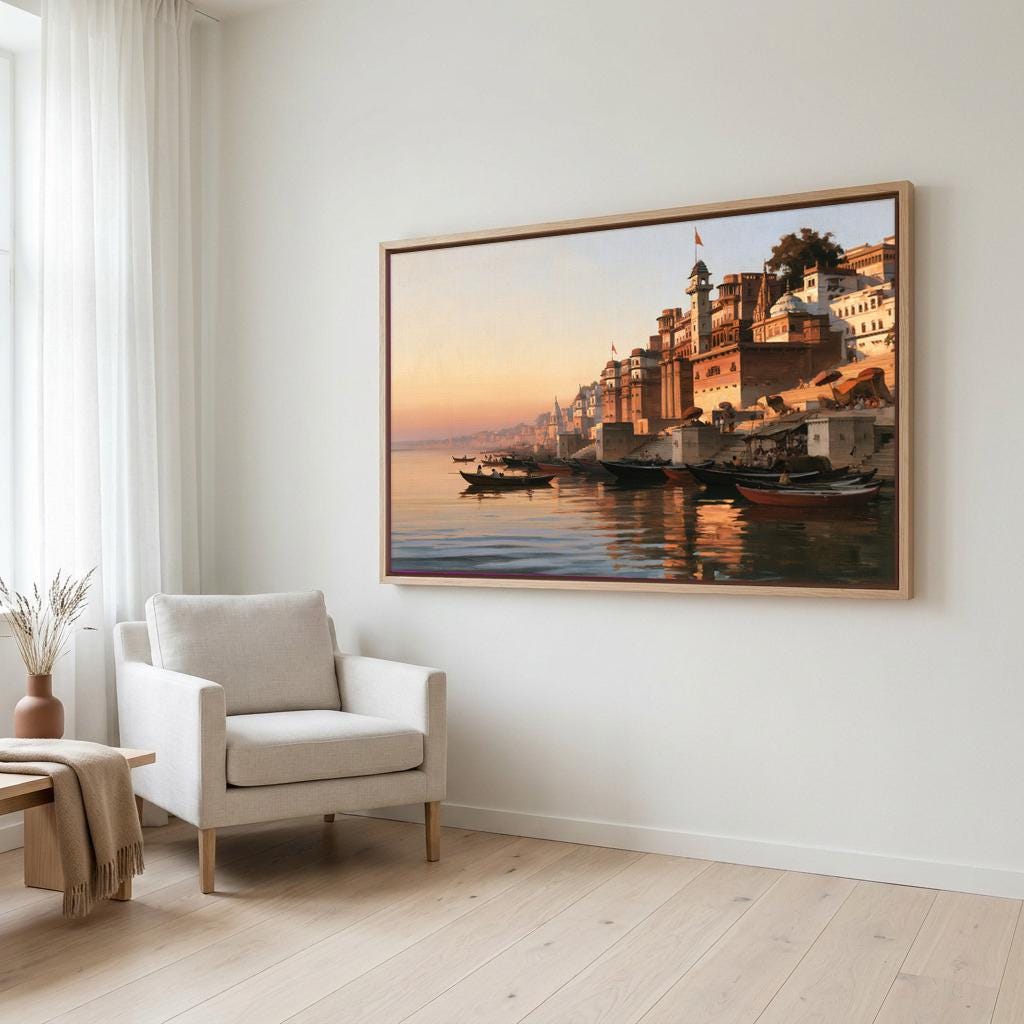a large, framed painting of a serene waterfront scene with boats and buildings reflected in the water. The painting is hung on a white wall in a room with a white chair and a wooden table.