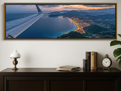A large framed photograph depicting a scenic coastal city at sunset, with the airplane wing visible in the top left corner.
