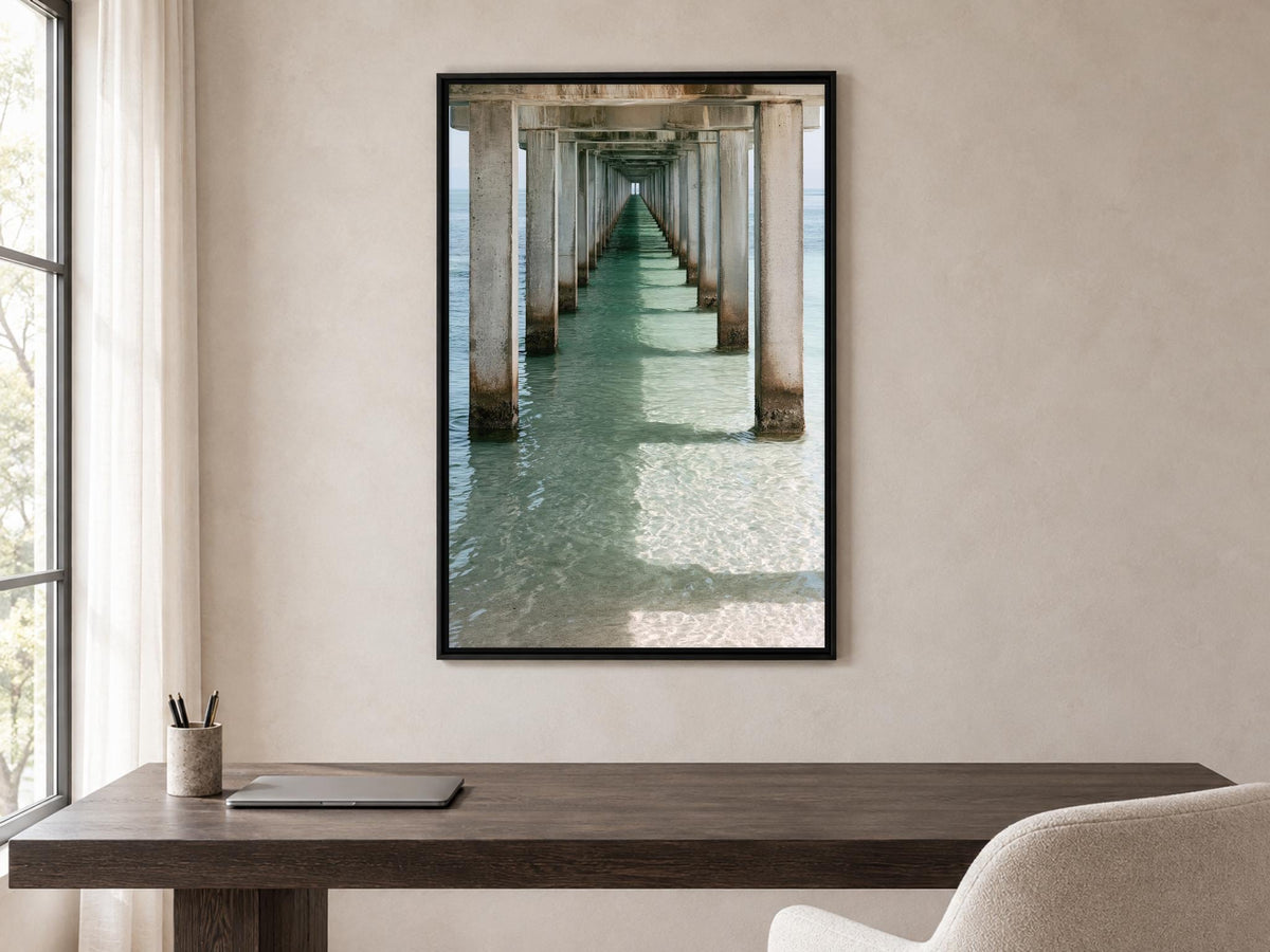 a framed photograph of a long pier extending into the water, with the pier's pillars and the water's surface creating a serene and tranquil atmosphere.