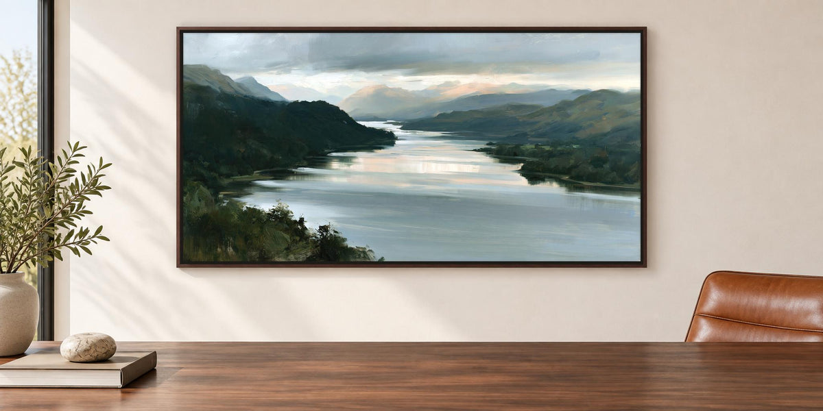 a large painting of a serene landscape with a river and mountains in the background, hanging on a wall above a wooden table.