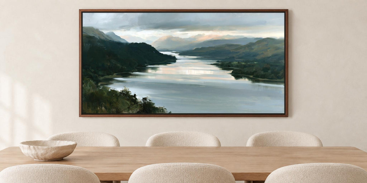 a large painting of a serene landscape with a river and mountains in the background, hanging on a wall above a wooden dining table with four chairs.