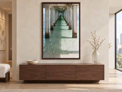 a large wooden cabinet with a bowl on top, situated in a modern living room with a large window overlooking a long pier.