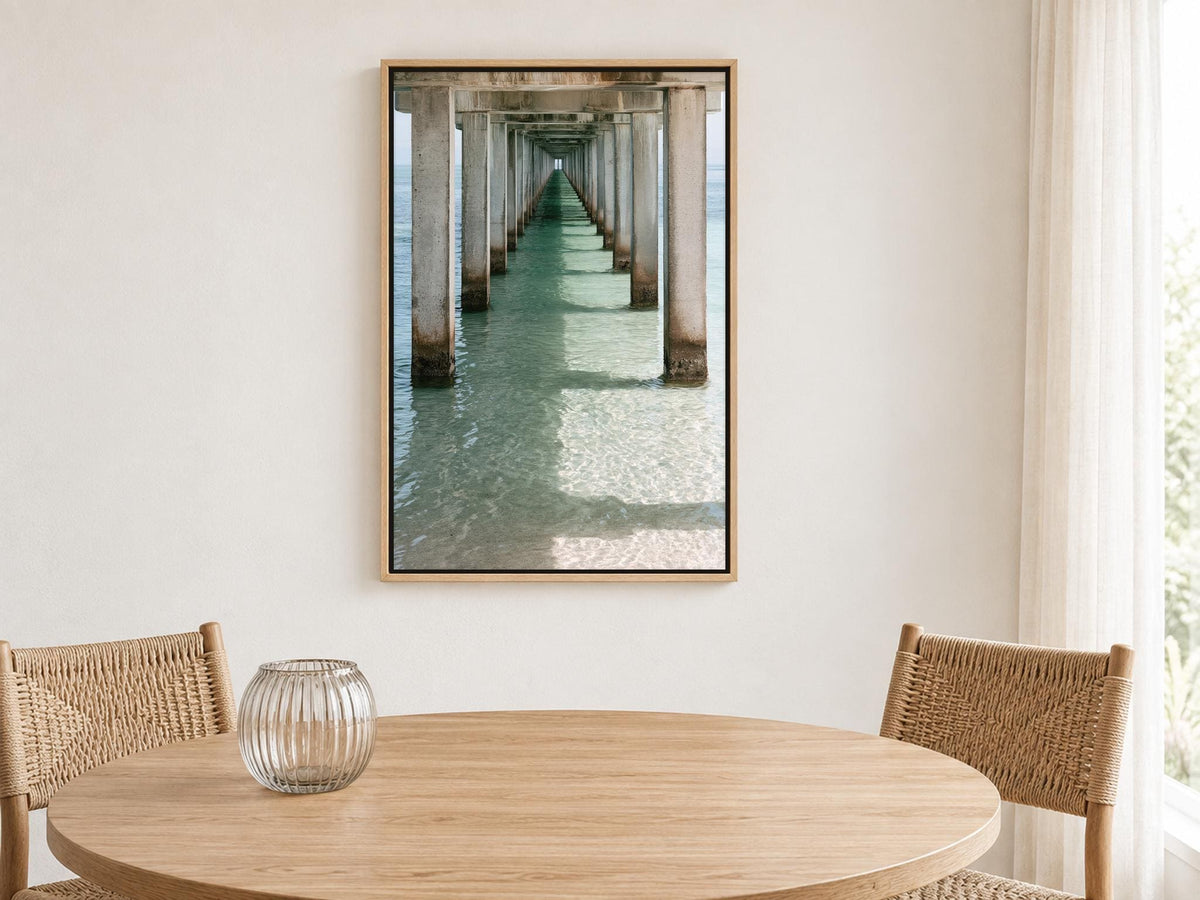 a wooden table with a glass vase on it, and a framed photograph of a long pier with pillars hanging on the wall above the table.