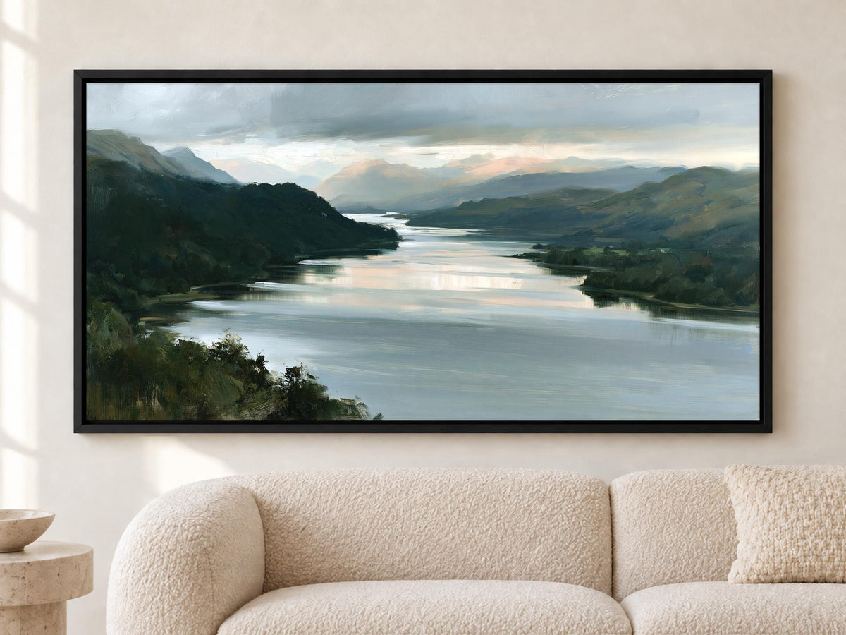 A large framed painting depicting a serene landscape with a river, mountains, and a cloudy sky hangs on a wall above a beige couch.