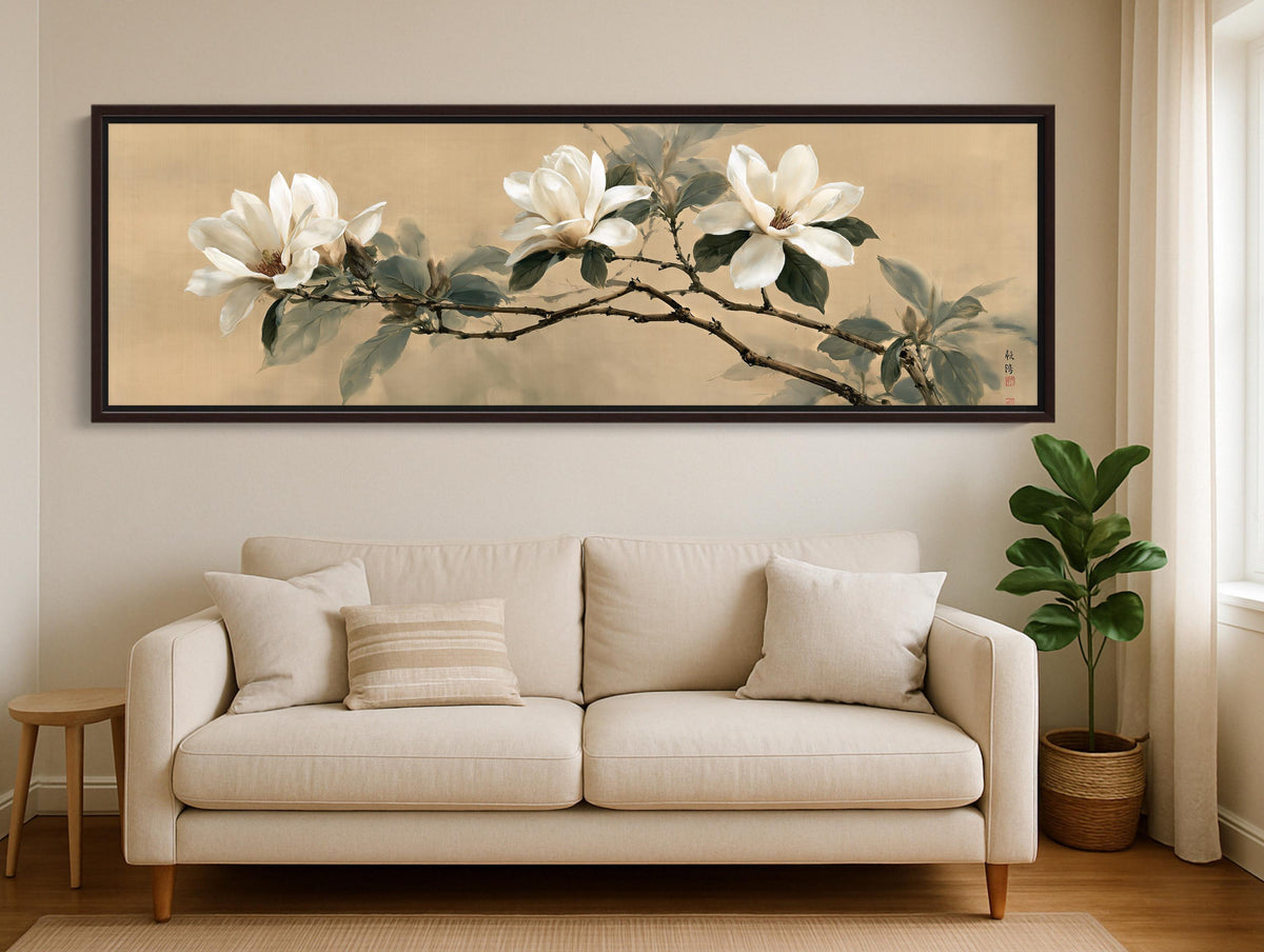 a large, framed painting of white flowers on a branch hanging on a wall above a beige sofa in a living room.