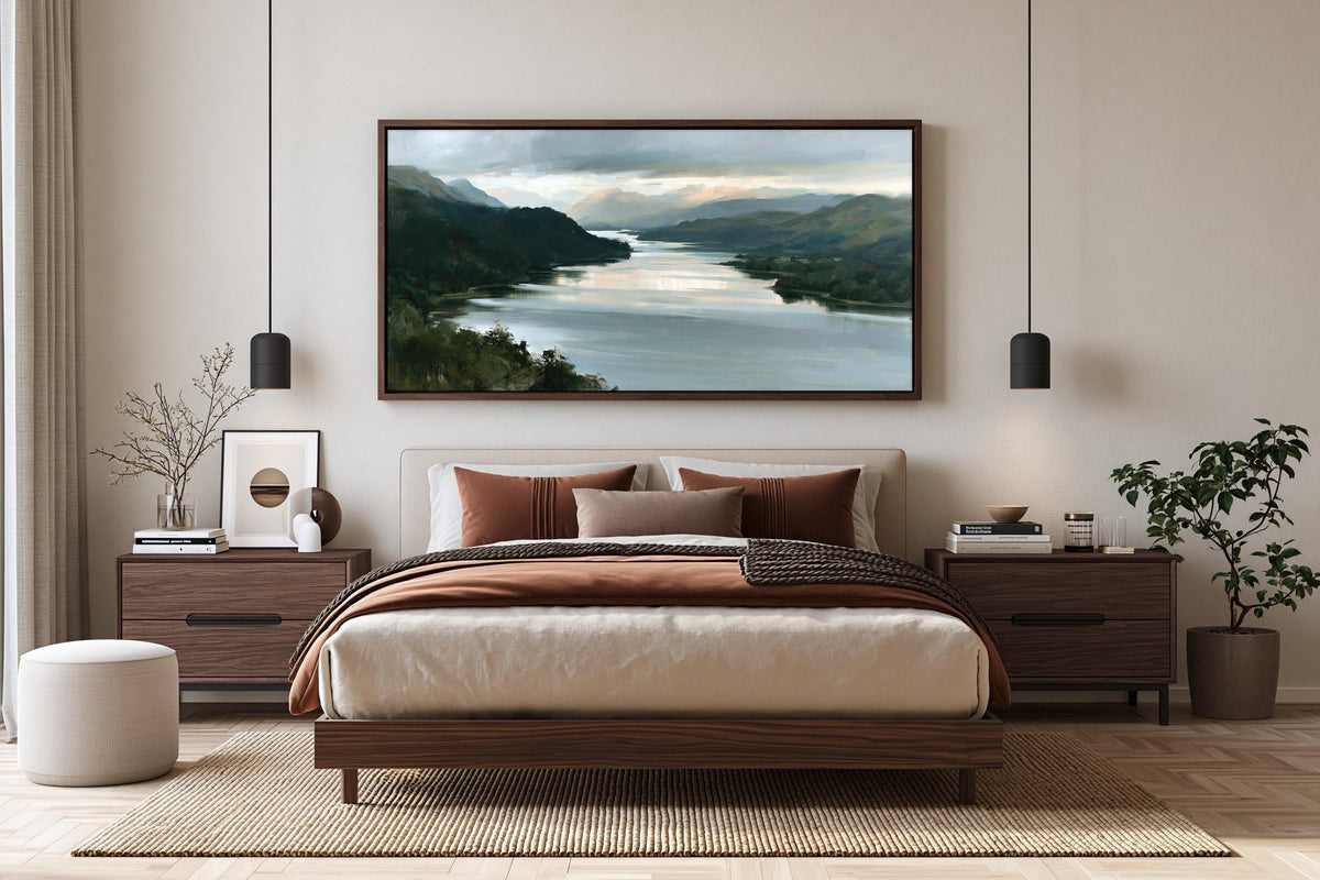 a serene bedroom with a large bed, wooden furniture, and a framed landscape painting hanging above it. The painting features a tranquil scene of a river surrounded by mountains, creating a peaceful and relaxing atmosphere.