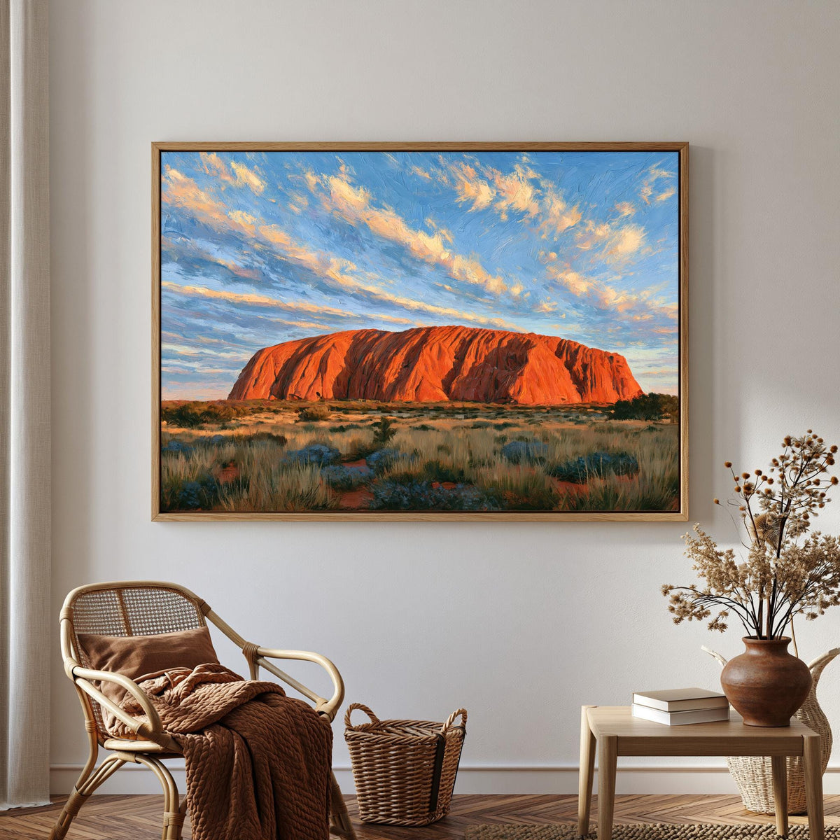 a large framed painting of Uluru, a famous red rock formation in Australia, hanging on a wall in a room with a wicker chair and a small table with a vase of flowers.