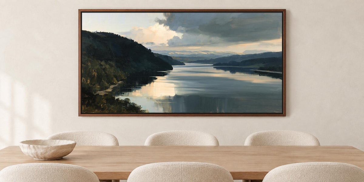 a large painting of a serene landscape with a calm lake and mountains in the background, hanging on a wall above a wooden dining table with four white chairs.