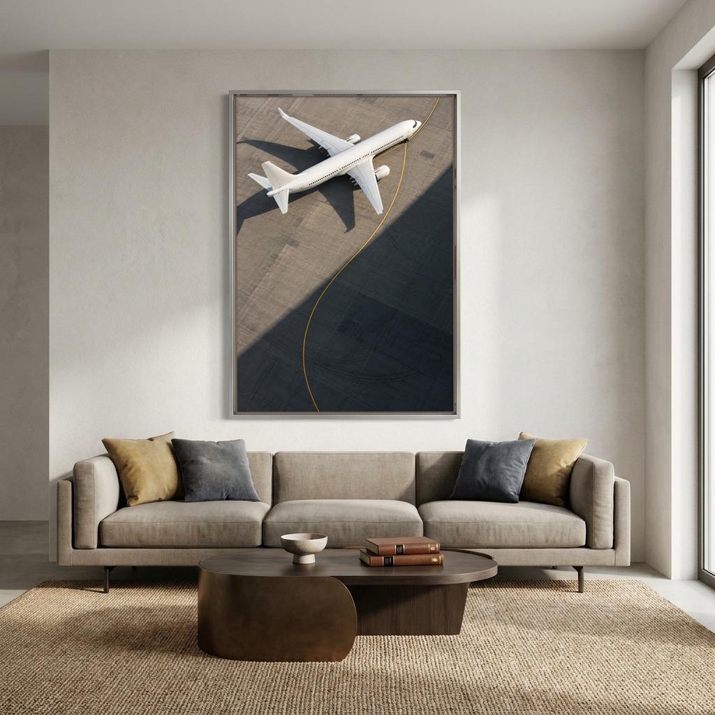 a large framed artwork depicting a white airplane on a runway, hanging on a wall above a beige sofa with two throw pillows.