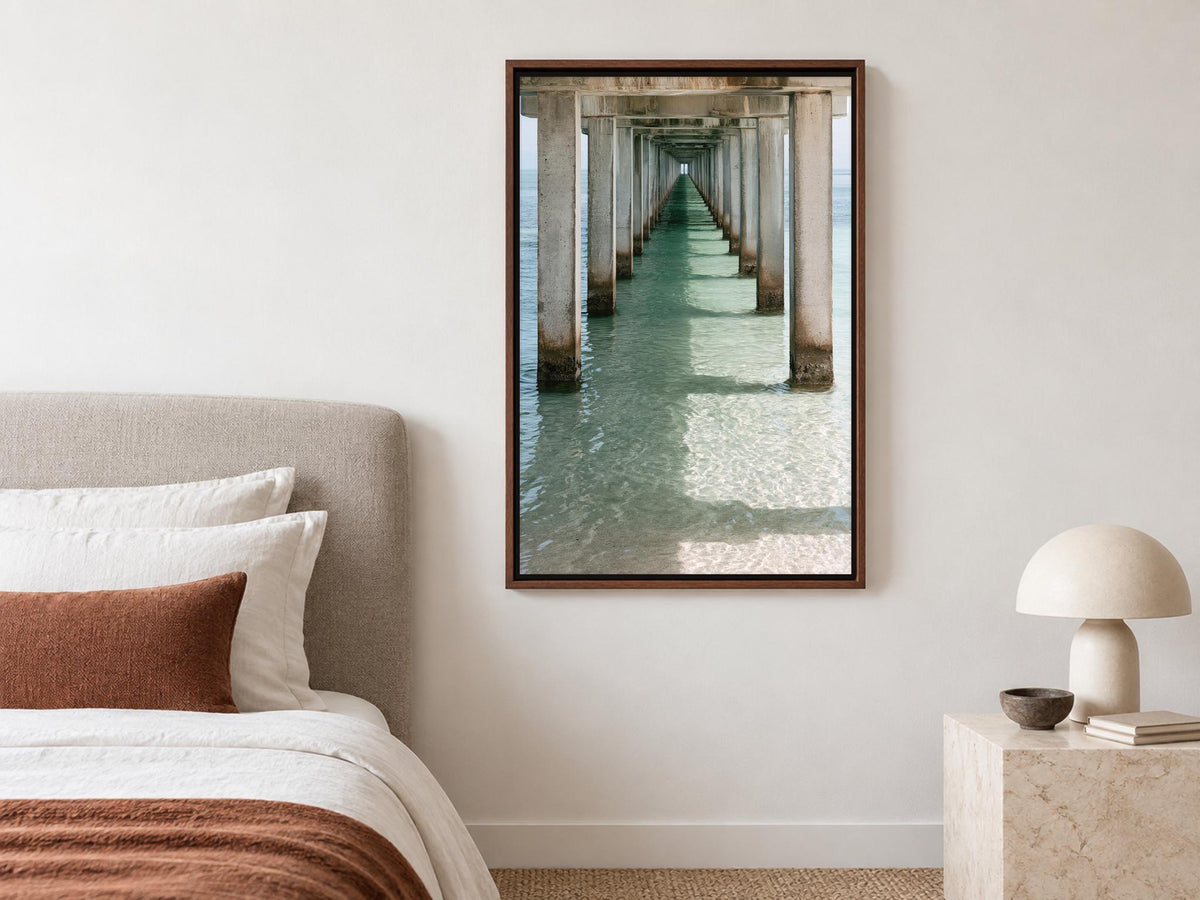 a serene bedroom scene with a bed, a lamp, and a framed photograph of a long pier extending into the water.