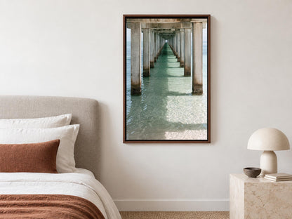 a serene bedroom scene with a bed, a lamp, and a framed photograph of a long pier extending into the water.