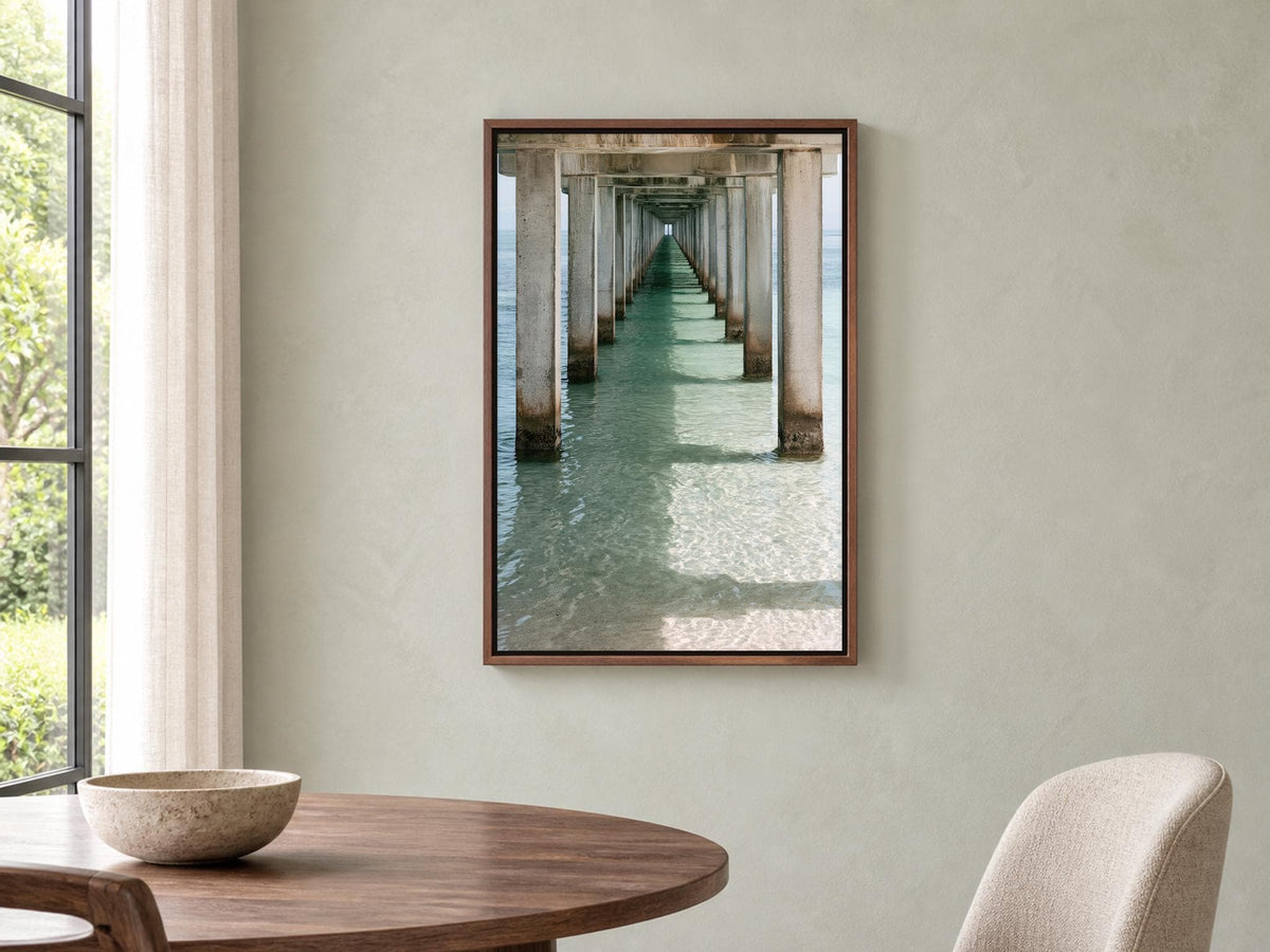 a wooden dining table with a bowl on it, and a framed photograph of a long pier with columns hanging on the wall above the table.