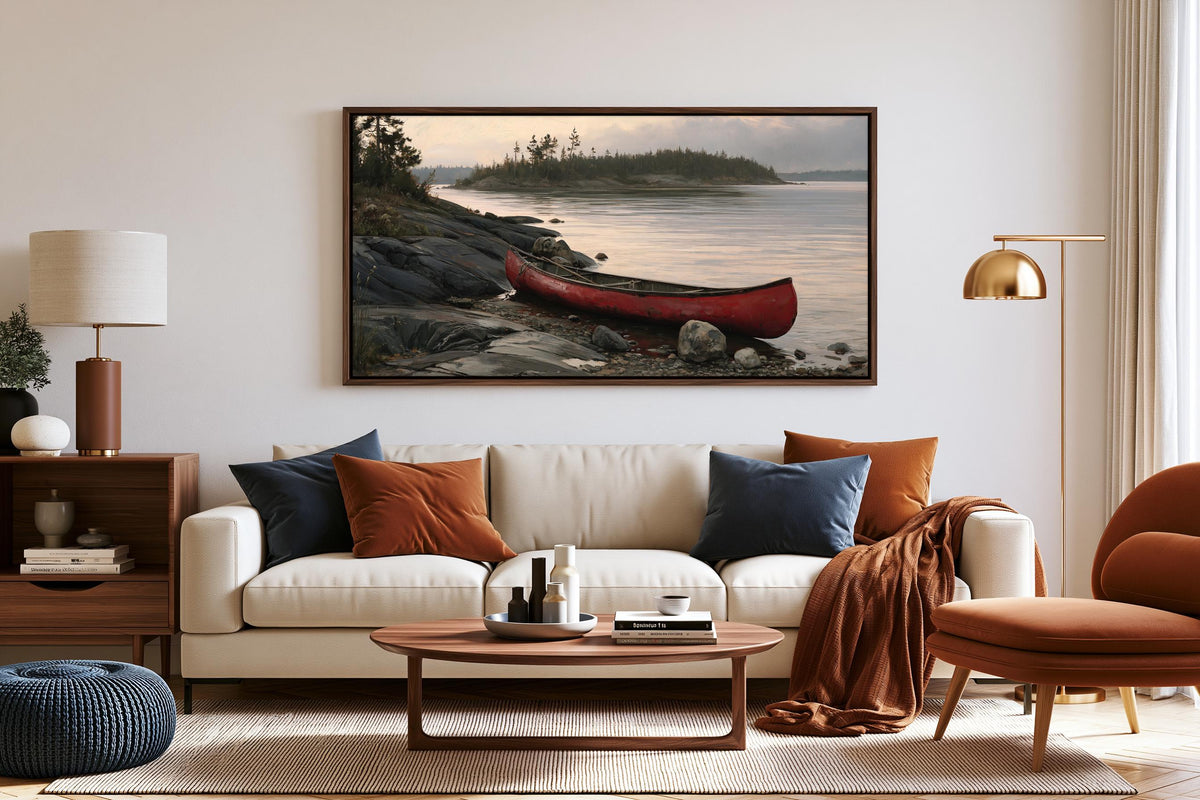 a living room with a white sofa, a wooden coffee table, and a large framed picture of a red canoe on a rocky shore.
