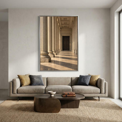 a modern living room with a large framed photograph of a classical architectural hallway with columns hanging on the wall above a gray sofa with two throw pillows.