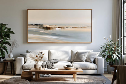 a serene living room with a large painting of a beach scene hanging on the wall above a white sofa. The sofa is adorned with a throw blanket and a vase of dried flowers. The room also features a wooden coffee table, a potted plant, and a large window that allows natural light to fill the space.