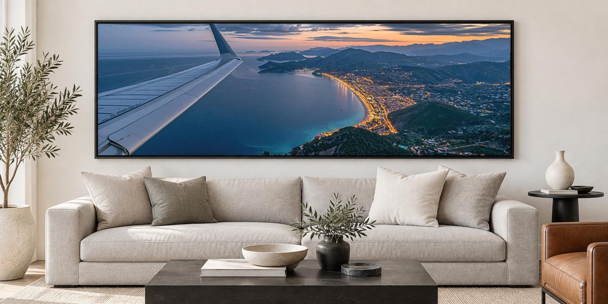 A large, framed photograph of an aerial view of a coastal city at sunset, with the wing of an airplane visible in the top left corner.