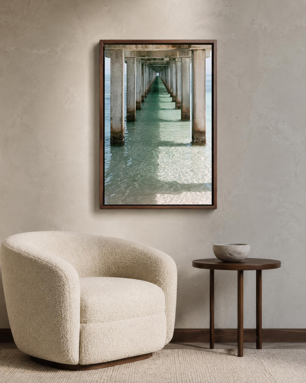 a cozy living room with a plush white armchair, a small round table, and a framed photograph of a long pier extending into the water.