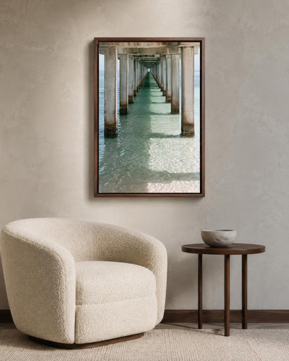 a cozy living room with a plush white armchair, a small round table, and a framed photograph of a long pier extending into the water.