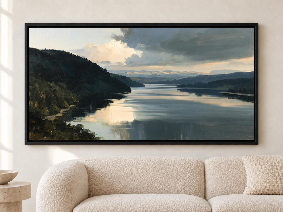 a large, framed painting of a serene landscape depicting a calm lake surrounded by mountains and hills.