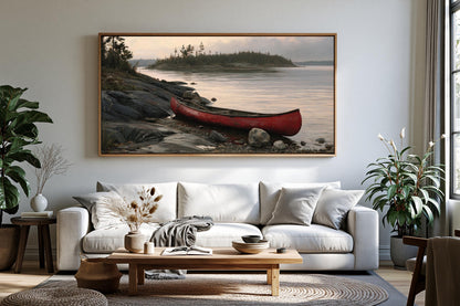 a large, framed painting of a red canoe resting on a rocky shore, with a serene lake and trees in the background. The painting is hung on a wall above a white sofa in a cozy living room setting.