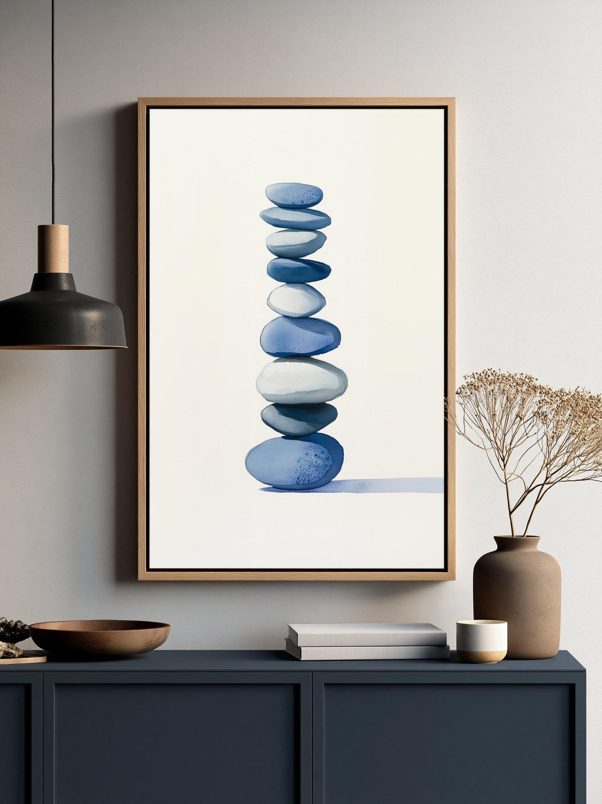 a framed artwork of blue and white stones arranged in a stack, hanging on a wall above a dark blue cabinet or shelf.