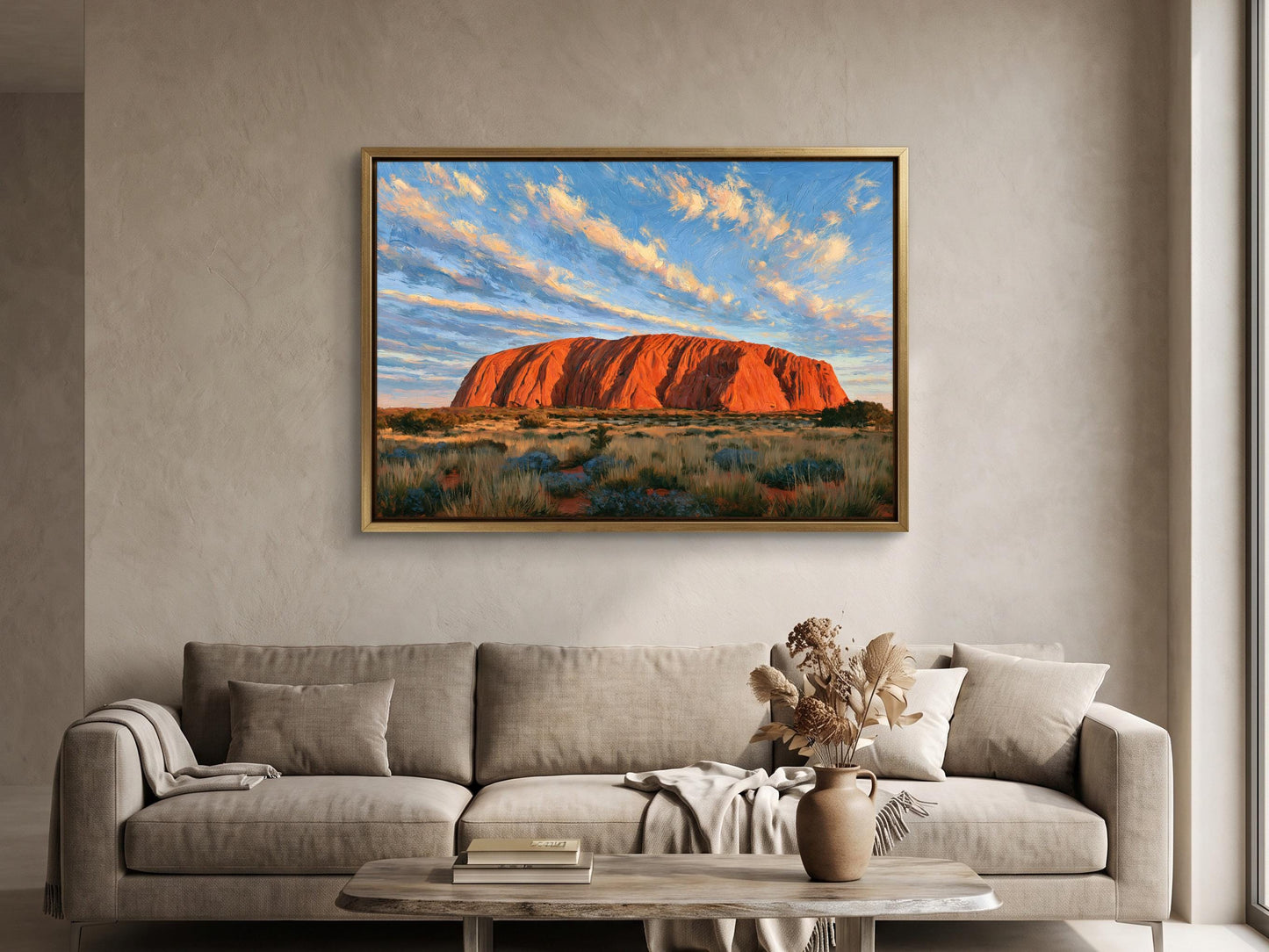 a large framed painting of Uluru, a famous red rock formation in Australia, hanging on a wall above a beige sofa in a living room.