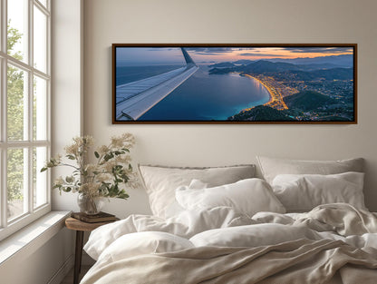 a large, framed picture of an airplane wing with a scenic view of a coastal city and mountains below.