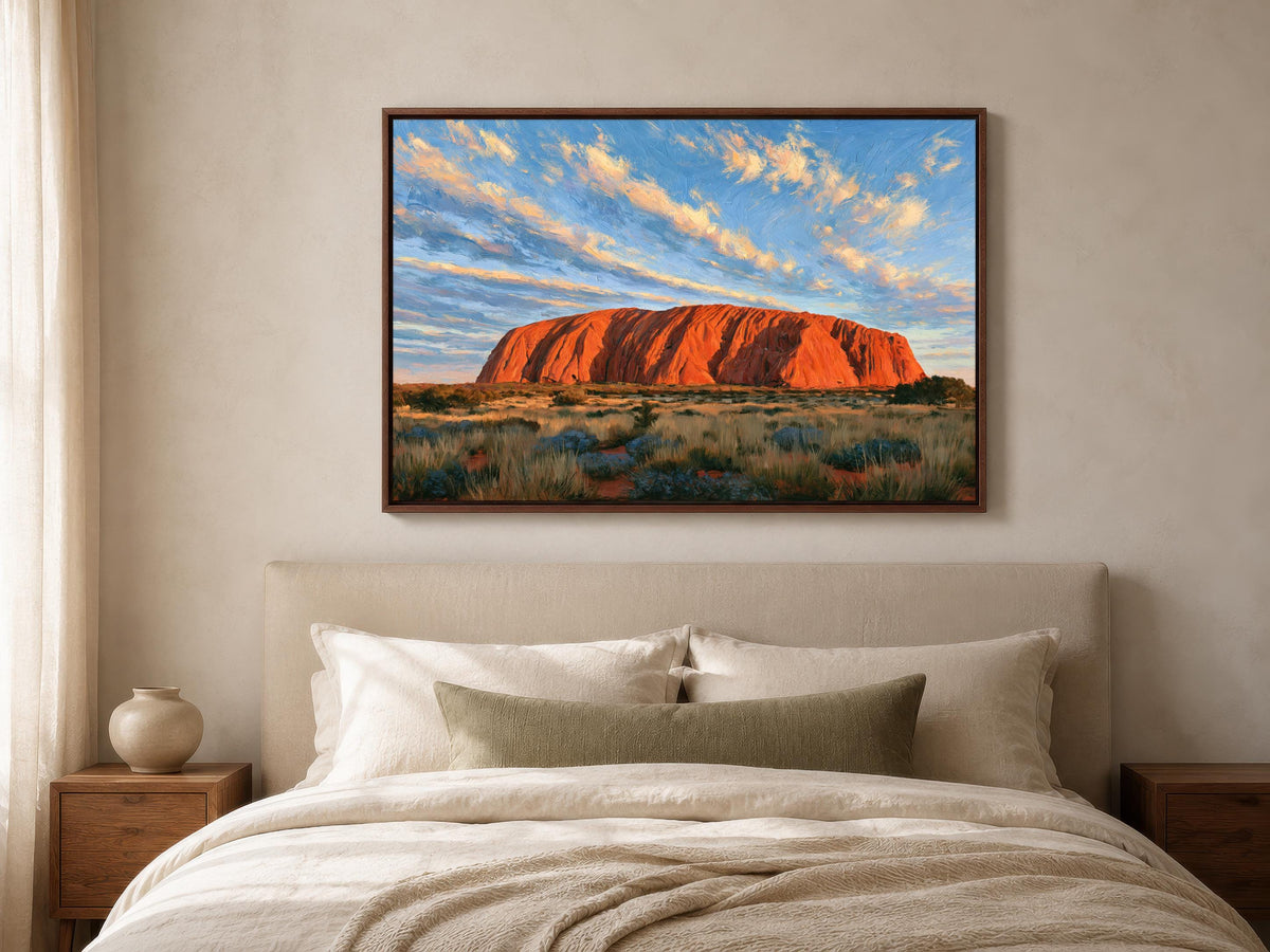 a large, framed painting of Uluru, a famous rock formation in Australia, hanging on the wall above a bed with white bedding.
