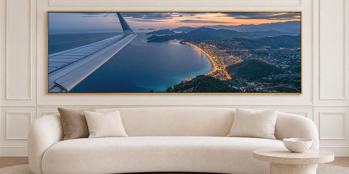 A large, framed aerial view of a coastal city at sunset, with the airplane wing visible in the top left corner.