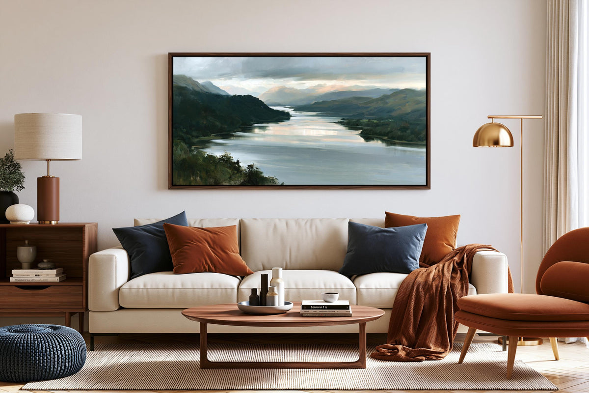 a cozy living room with a large painting of a serene landscape hanging on the wall above a white sofa adorned with throw pillows. The room is furnished with a wooden coffee table, a brown armchair, and a wooden side table with a lamp. The overall decor and arrangement create a warm and inviting atmosphere.