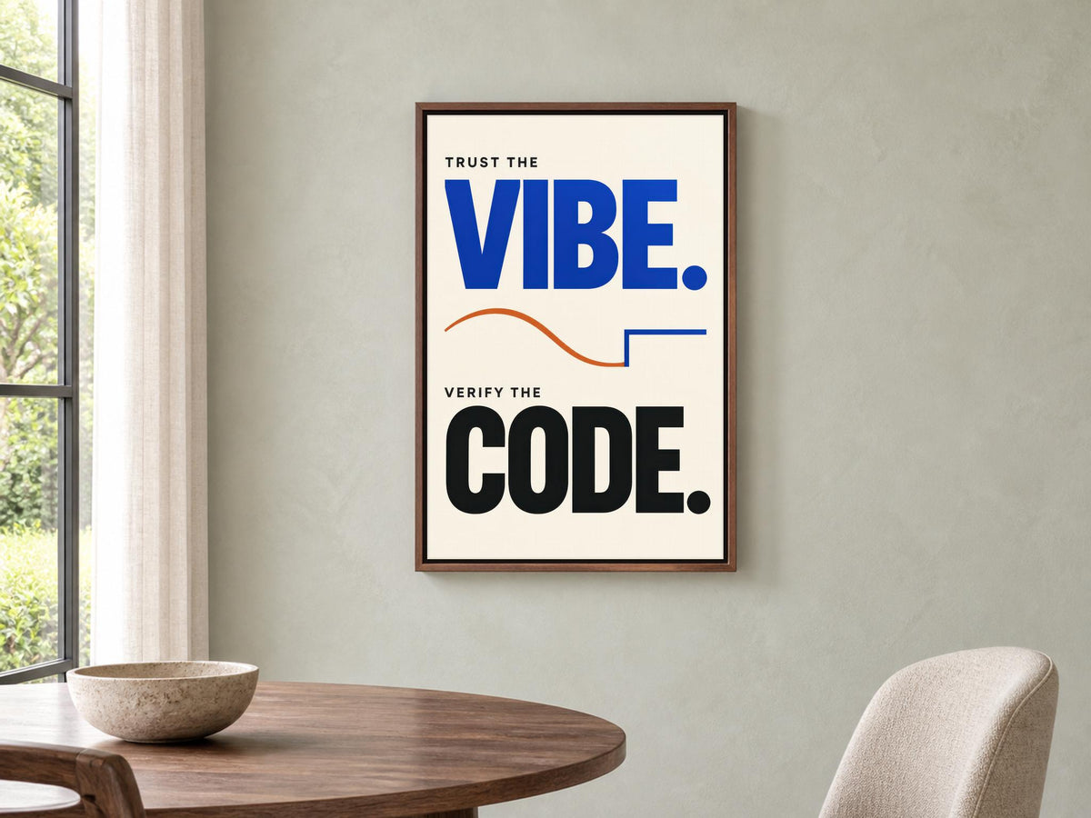 a framed poster with the text "Trust the VIBE. VERIFY the CODE." displayed on a wall above a wooden table and chair.