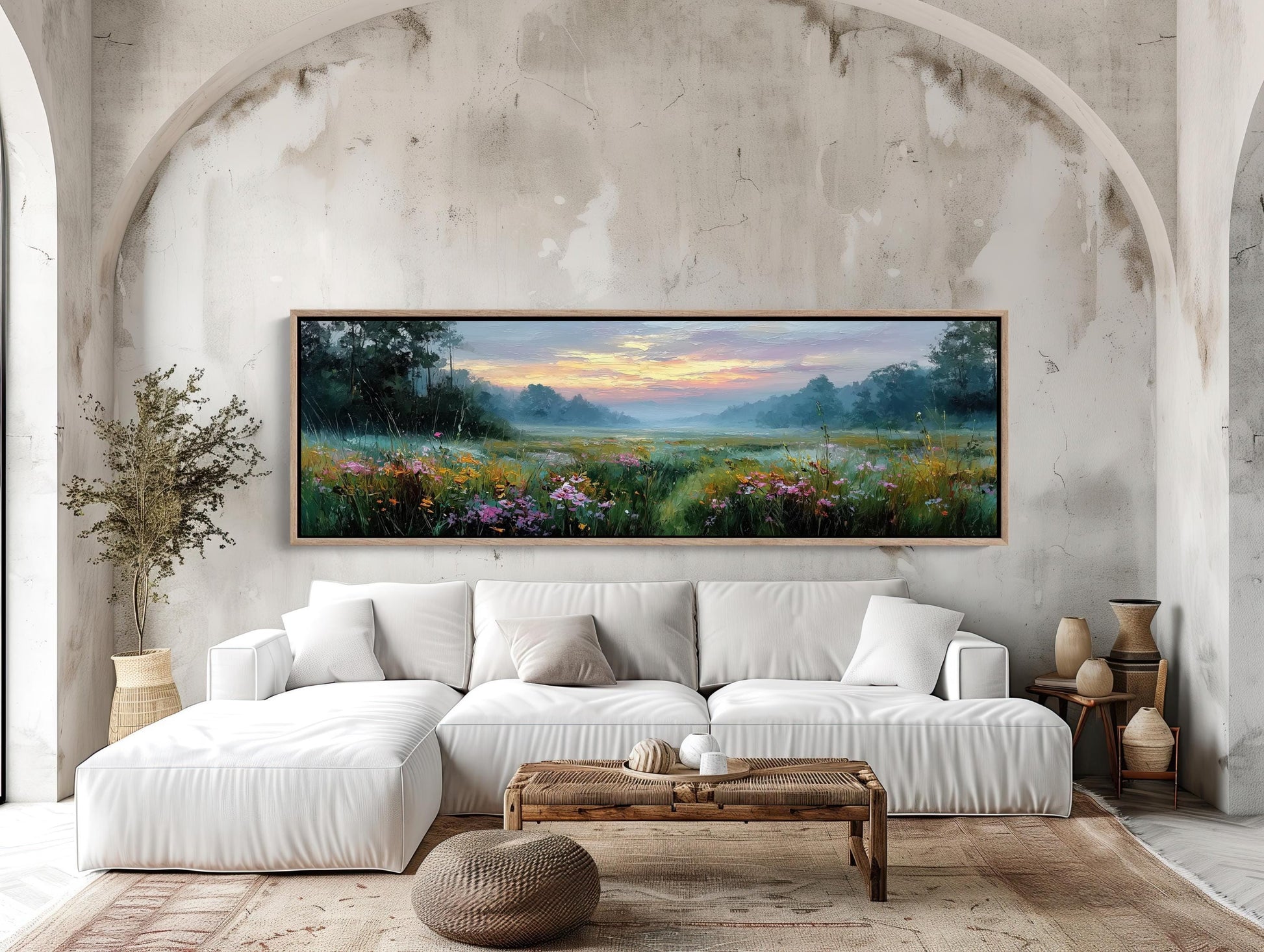 a large, framed painting of a serene landscape with a field of flowers and a colorful sky above. The painting is hung on a wall above a white sofa, which is positioned in front of a wooden coffee table. The room has a modern and minimalist design, with a rug on the floor and some decorative elements such as vases and a potted plant.