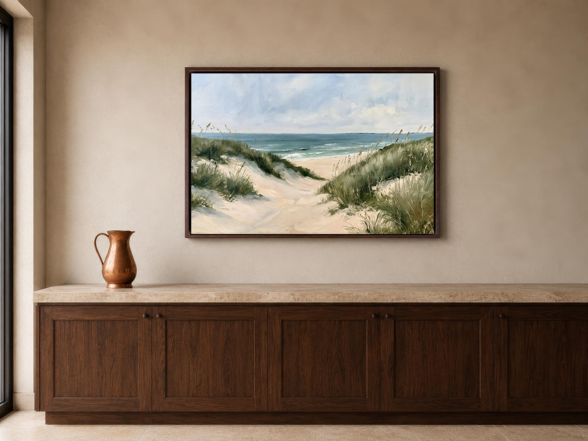 a large framed painting of a beach scene hanging on a wall above a wooden cabinet or counter.
