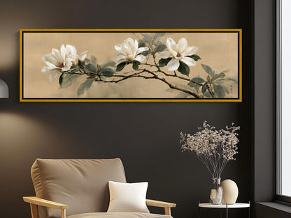 a large framed painting of white flowers on a branch hanging on a wall above a beige armchair in a living room setting.