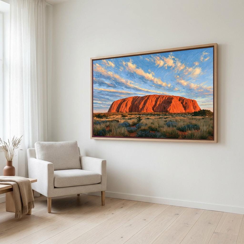 a large framed painting of Uluru, a famous red rock formation in Australia, hanging on a white wall in a living room.